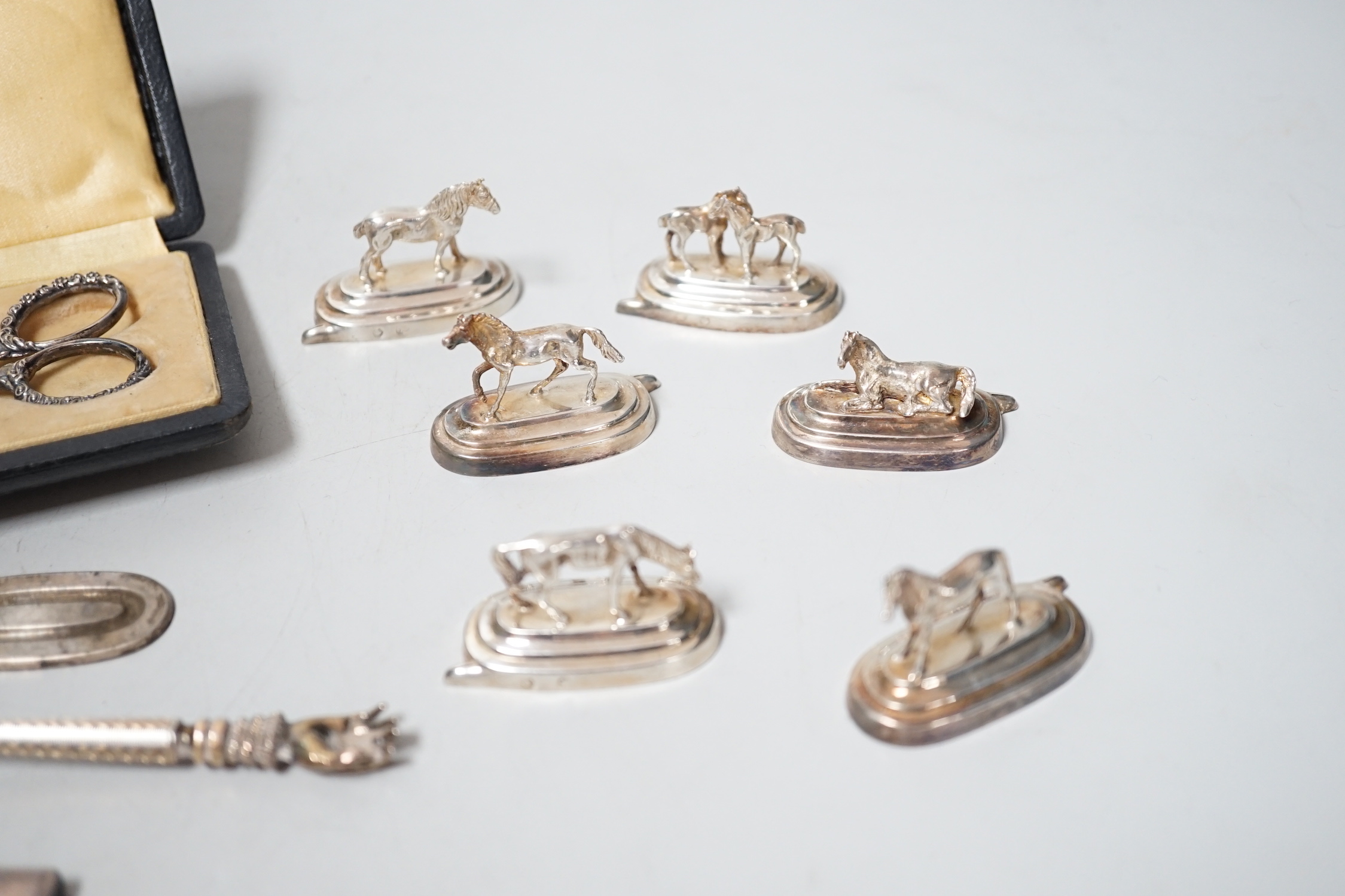 Six assorted Spanish white metal horse menu holders, 43mm, a cased necessaire set, a cigar cutter and a French white metal spoon with hand terminal.